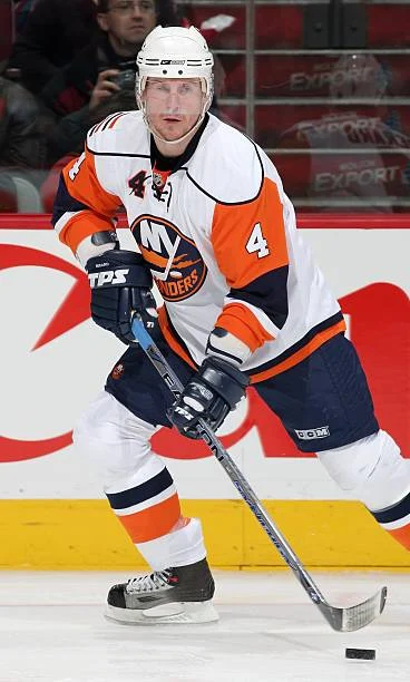 A hockey player is holding his stick while wearing an orange and white uniform.