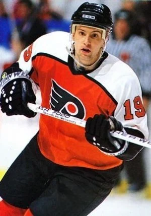 A man in an orange and black uniform holding a hockey stick.