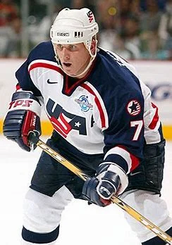 A man in white and blue hockey uniform holding a stick.